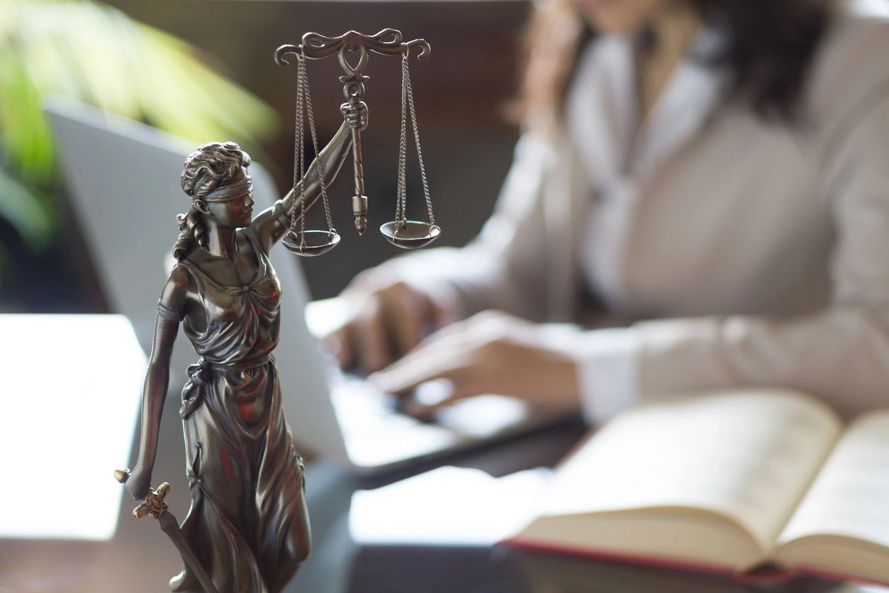 Lady Justice statue with a blurred legal professional working in the background.